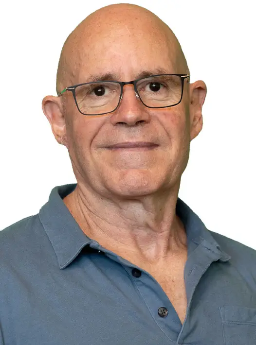 A man wearing glasses and a gray polo shirt sitting in a relaxed pose, looking directly at the camera with a neutral expression.