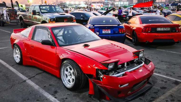 A heavily modified red Nissan 180SX, a JDM drift car, showing its rugged charm in a vibrant parking lot setting.