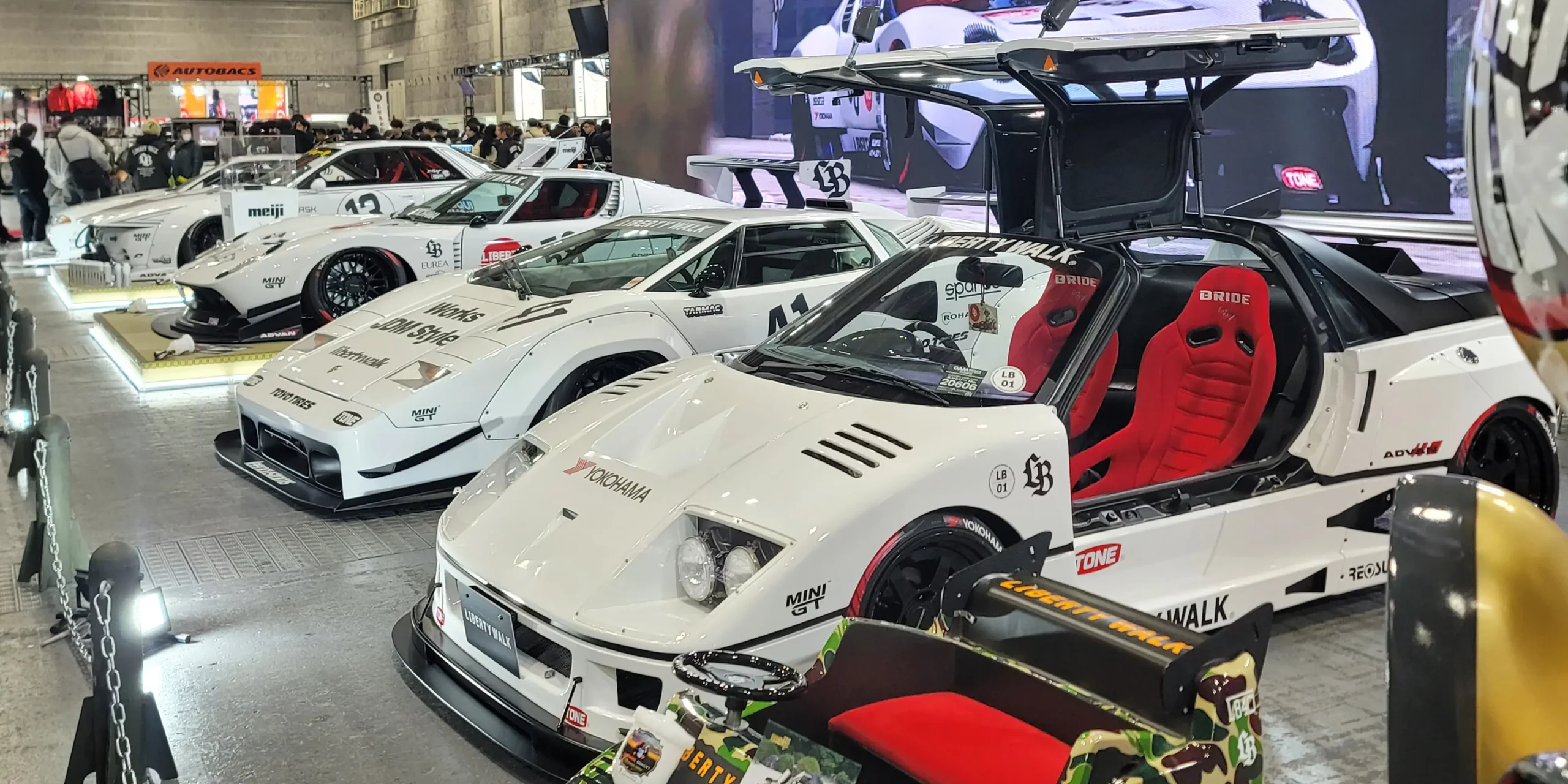 A lineup of custom cars by Liberty Walk. Wide-body tuned cars showcased in a powerful and eye-catching booth.