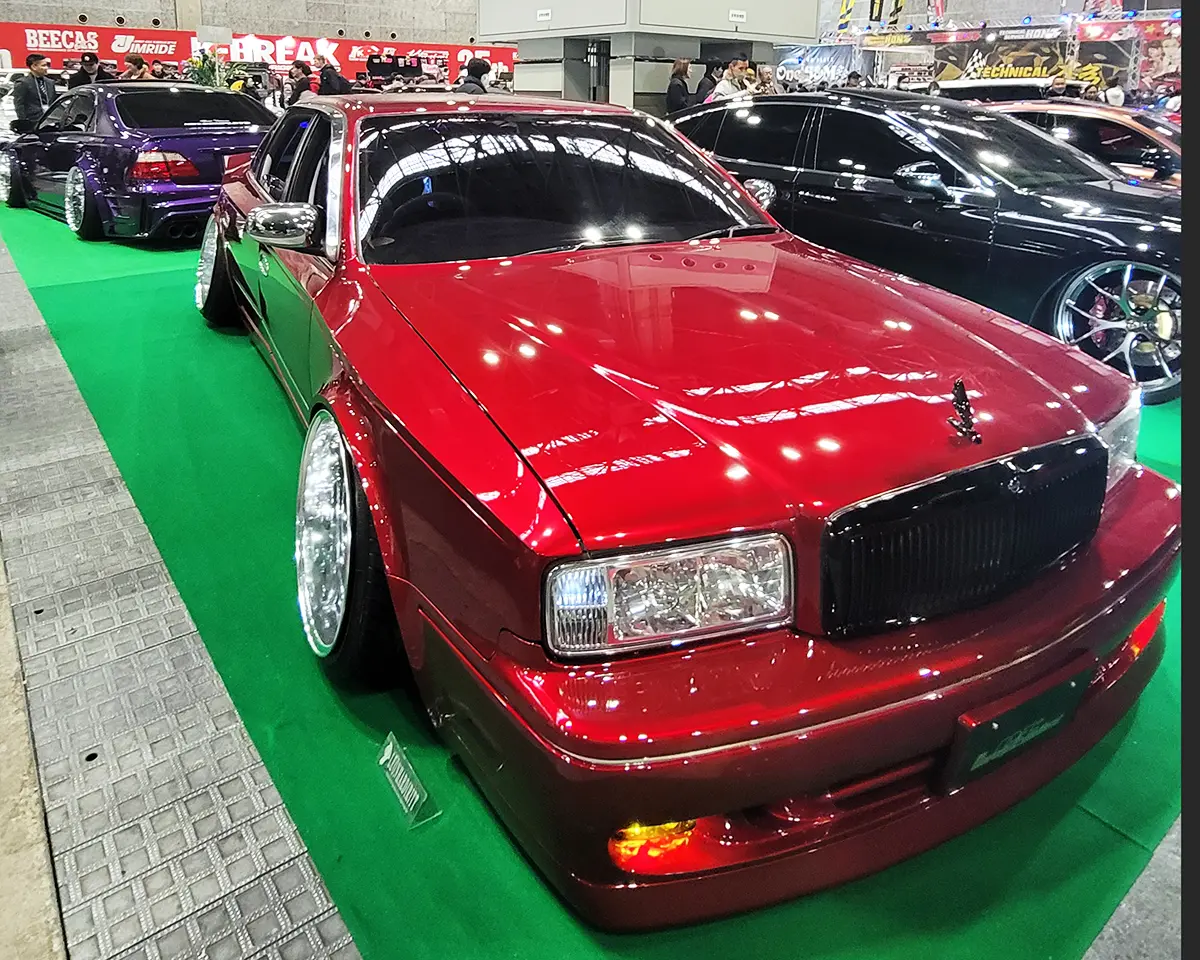 A stunning Nissan Gloria in deep red, featuring wide-body modifications and an aggressive stance.