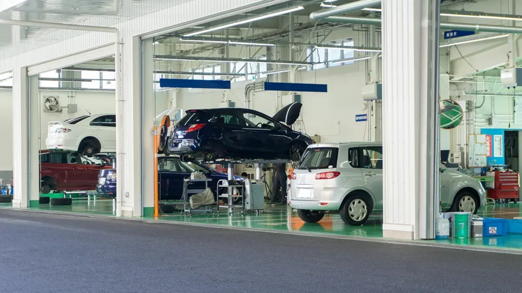 A vehicle inspection and maintenance garage with multiple cars being serviced, including vehicles lifted on hydraulic platforms.